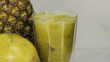 copo de vidro com suco revitalizante, ao lado de um abacaxi e um maracujá