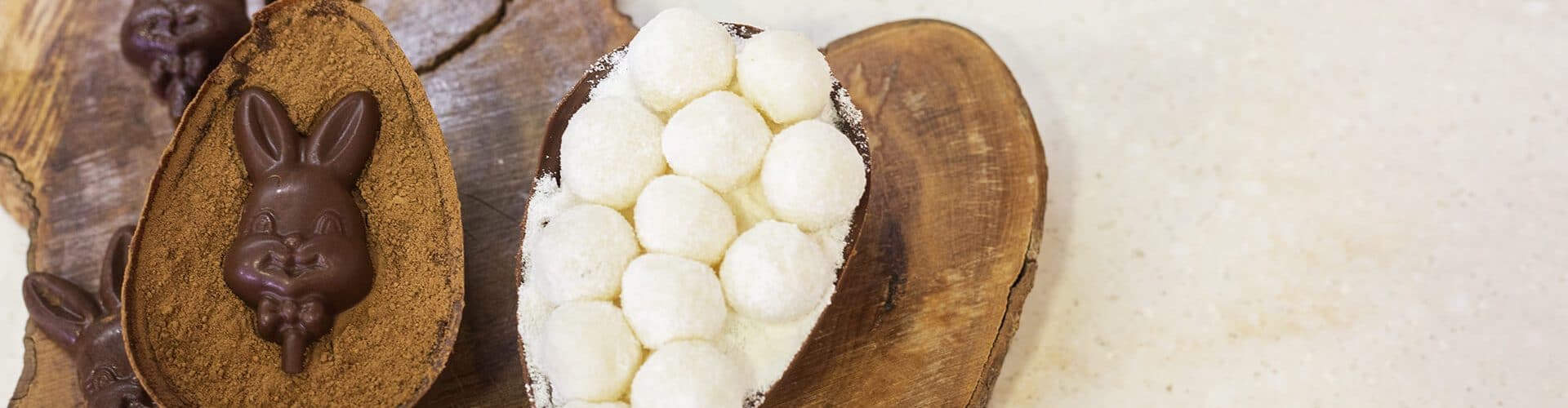 duas metades de ovos de páscoa recheadas com chocolate decorado, em uma tábua de madeira