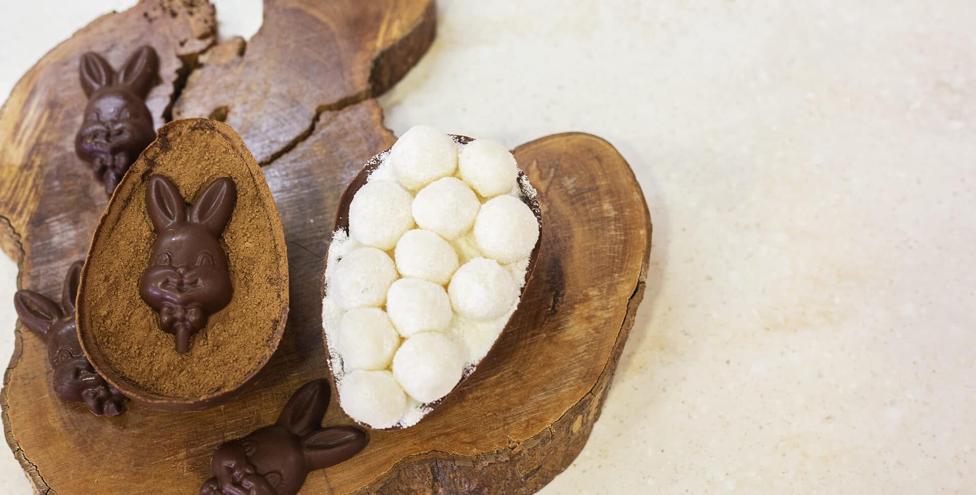 duas metades de ovos de páscoa recheadas com chocolate decorado, em uma tábua de madeira