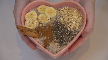 Mãos segurando bowl em forma de coração com mingau de aveia com banana