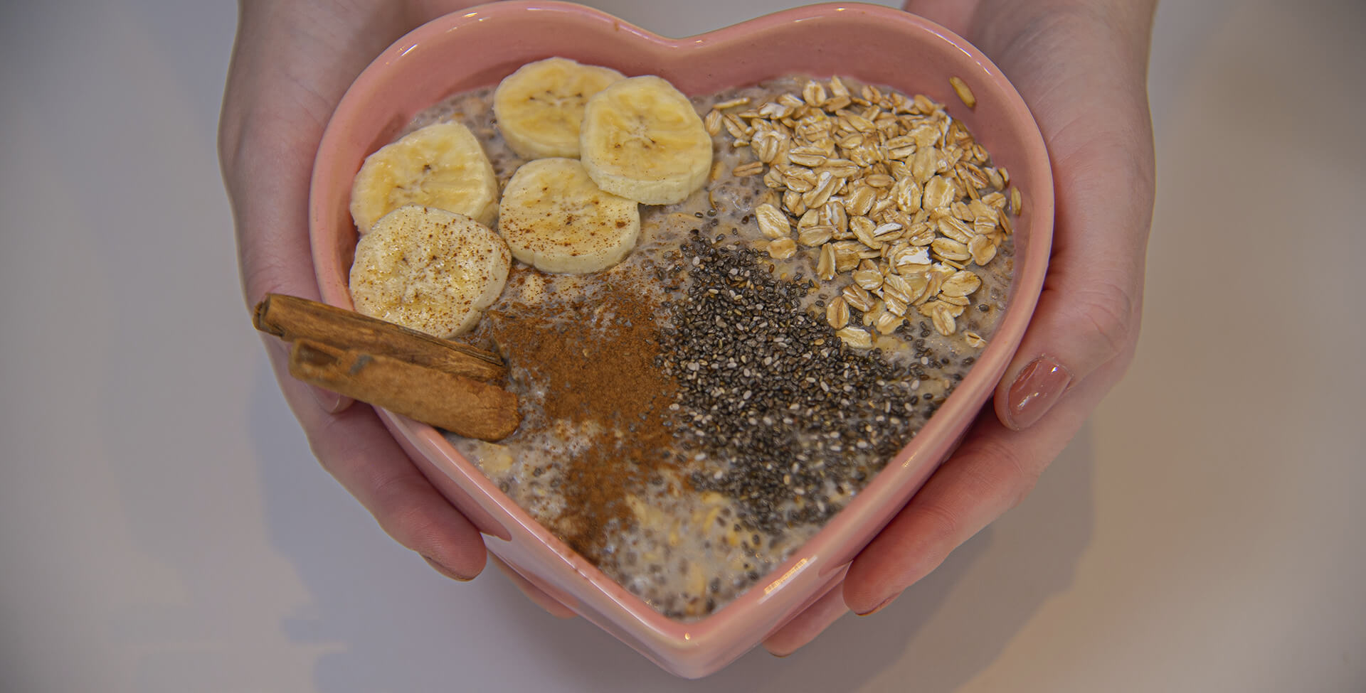 Mãos segurando bowl em forma de coração com mingau de aveia com banana