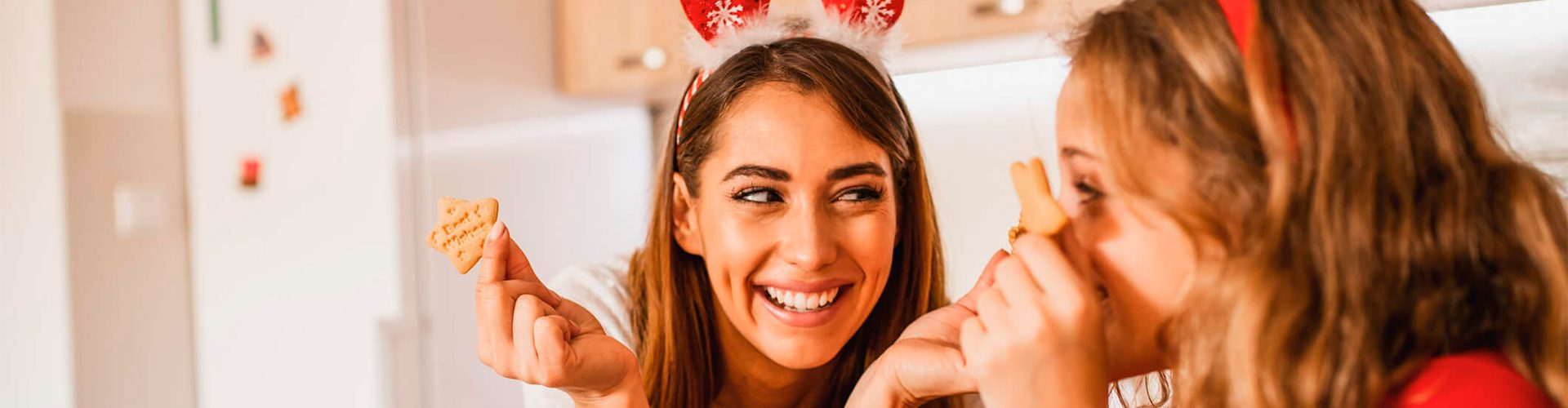 mãe e filha preparam receitas de natal. Elas estão sorrindo e segurando biscoistos de natal