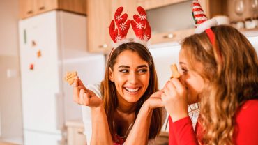 mãe e filha preparam receitas de natal. Elas estão sorrindo e segurando biscoistos de natal