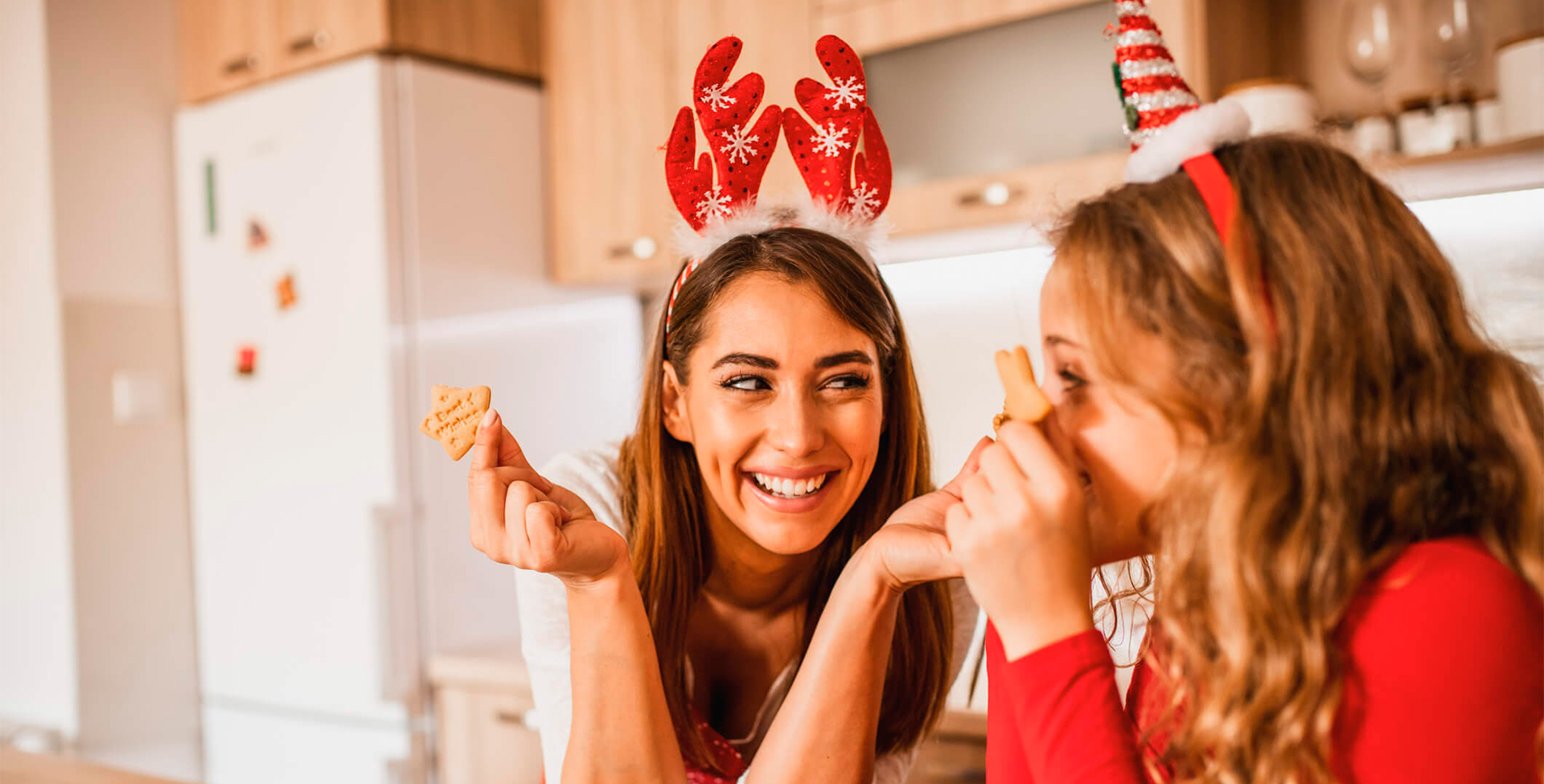 mãe e filha preparam receitas de natal. Elas estão sorrindo e segurando biscoistos de natal