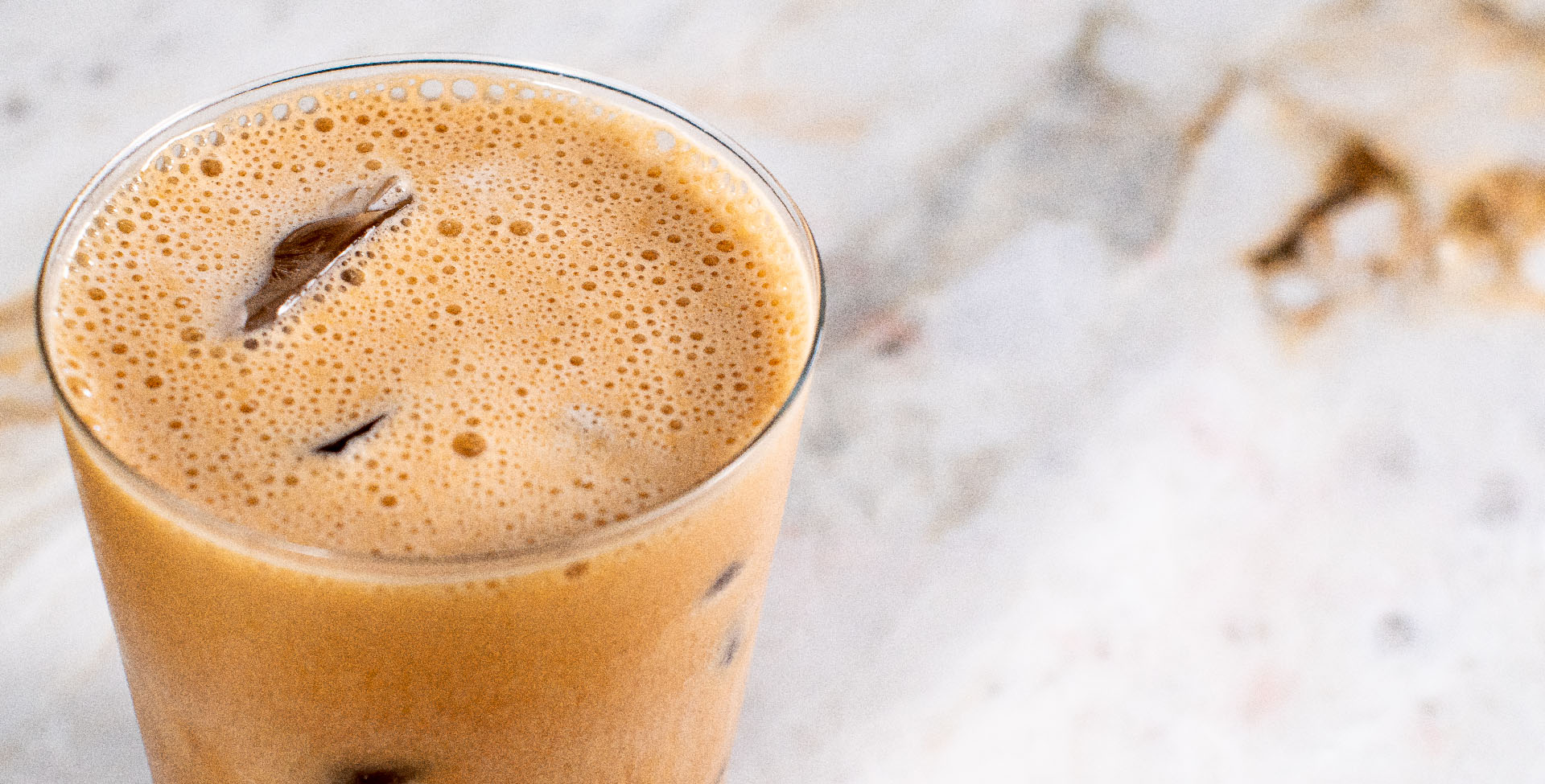 Um copo de vidro com café proteico gelado, em cima de uma bancada de mármore.